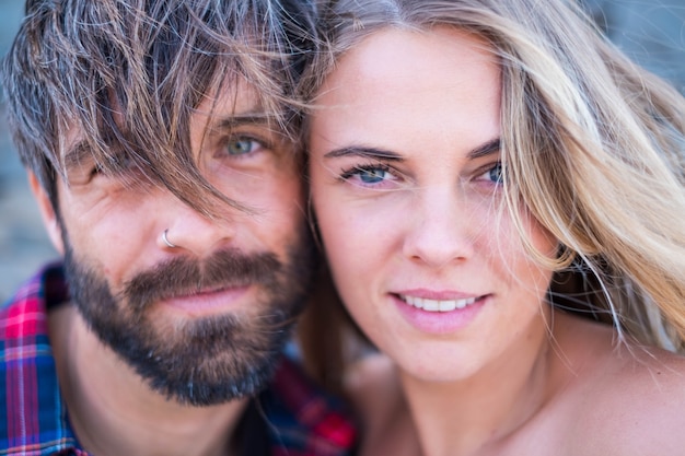 Close-up e retrato de um homem bonito e bonito e uma mulher juntos com seus rostos próximos um do outro olhando para a câmera sorrindo - mulher desanimada com olhos azuis e homem bonito com olhos verdes