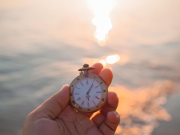 Close-up einer vintage Taschenuhr in weiblicher Hand mit dem Meer im Sonnenuntergang als Hintergrund