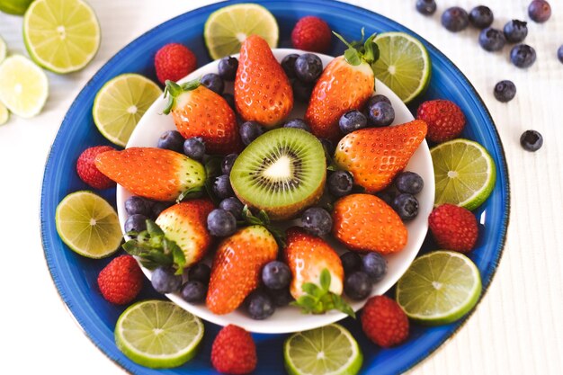 Close-up em um prato azul cheio de morangos e mirtilos com meio kiwi. Conceito de alimentação e dieta saudável