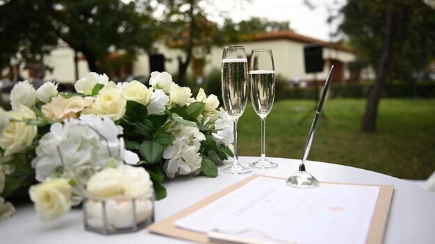 Close-up, em uma mesa redonda de madeira branca em um dia de sol, há uma linda caixa de vidro multifacetada, decorada com flores, para alianças de casamento