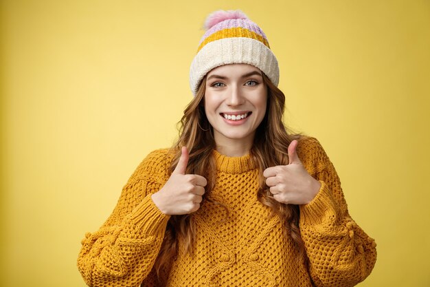 Close-up encantadora simpática jovem mostrando gesto de polegar para cima sorrindo aprovação gostando da sua ideia encorajar continue, satisfeito, boa escolha excelente, em pé, satisfeito, fundo amarelo