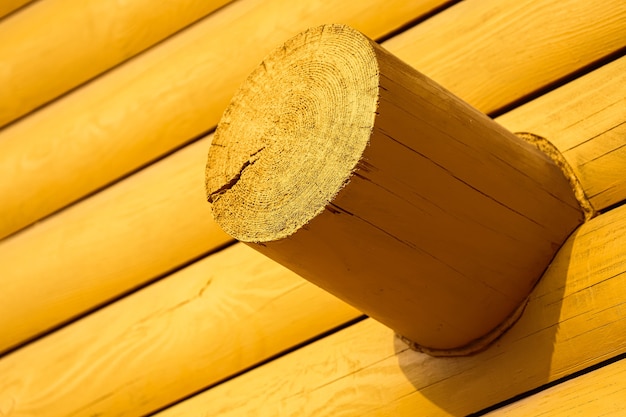 Close-up de una esquina de una casa de madera amarilla con troncos redondos