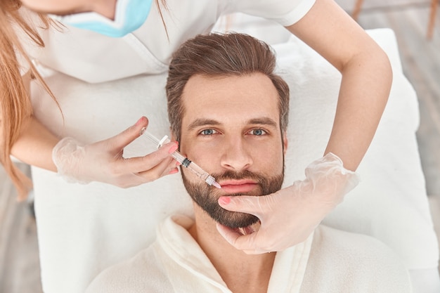 Foto close up faz injeções de mesoterapia no homem barba. tratamento do sexo masculino por esteticista para crescimento de cabelo.