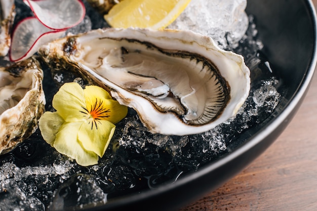 Close up Fine de Claire Oyster y limón servidos en un tazón negro con hielo en la mesa de madera.