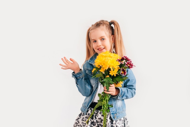 Close up, foco seletivo. Uma menina loira segurando crisântemos e gérberas nas mãos sobre um fundo branco, uma menina sorrindo e segurando flores da primavera nas mãos