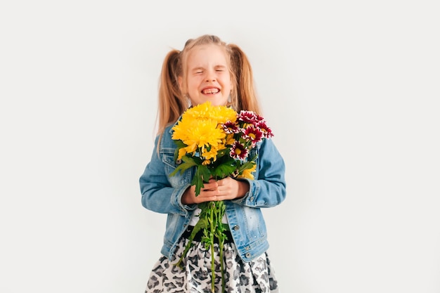 Close up, foco seletivo. Uma menina loira segurando crisântemos e gérberas nas mãos sobre um fundo branco, uma menina sorrindo e segurando flores da primavera nas mãos