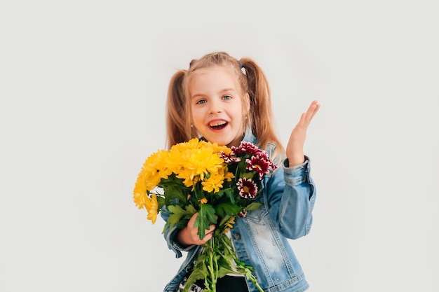 Close up, foco seletivo. Uma menina loira segurando crisântemos e gérberas nas mãos sobre um fundo branco, uma menina sorrindo e segurando flores da primavera nas mãos