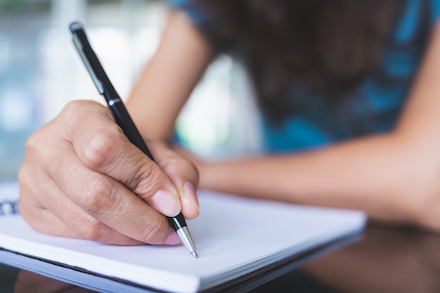 Close-up fotos de mulheres usando uma caneta preta para escrever em um caderno em branco sobre uma mesa de vidro