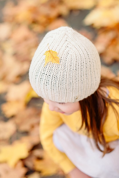 Close-up de un gorro de punto con una hoja amarilla otoñal caída sobre una linda chica en el otoño
