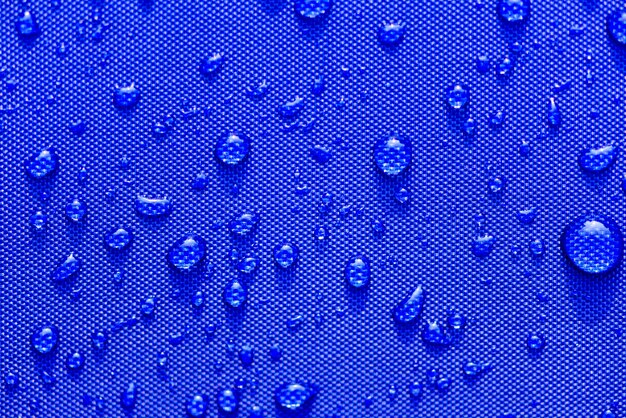 Close-up gotas de água padrão sobre um fundo de pano azul impermeável