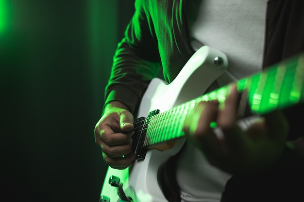 Foto close up hände junger mann rocker spielt e-gitarre auf der bühne live im konzert. mit neonlicht. junger mann, der in der show heavy-metal-musik und sologitarre übt.