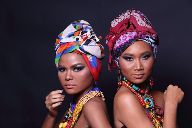 Close Up halben Körper der 20er Jahre asiatische zwei Frau mit Mode bilden African Hill Tribe Style. Gebräunte Hautmädchen drücken sich stark aus, lächeln, glücklich mit buntem ethnischem Accessoire auf schwarzem Hintergrund