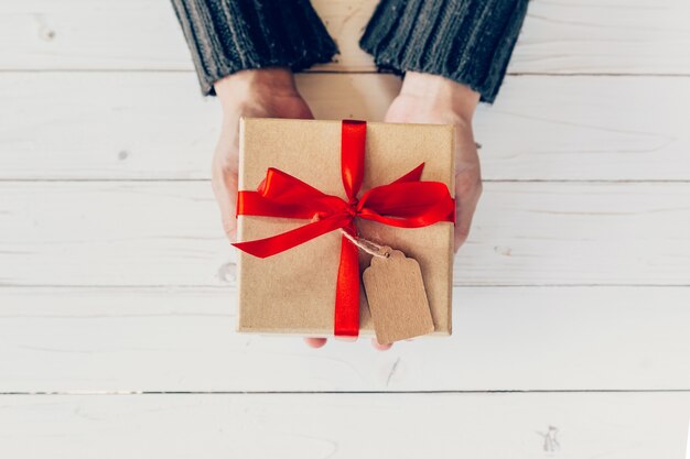 Close up Hand Frau halten und Person Geschenk-Box auf Holz Tisch für Neujahr Hintergrund.