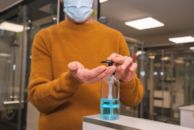 Close-up de un hombre irreconocible con una máscara desinfectando sus manos con alcogel en una tienda