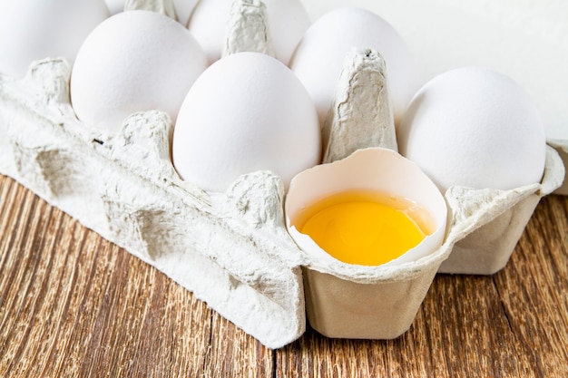 Close-up de huevos de gallina en la bandeja de papel y yema de huevo sobre madera