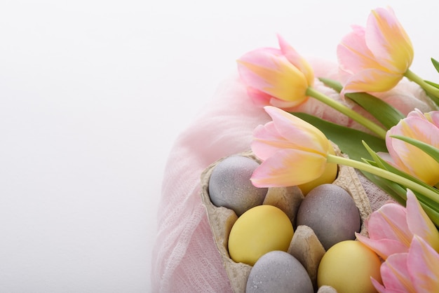 Close-up de huevos de Pascua azul y amarillo pastel con tulipanes rosados con una servilleta de tela rosa sobre fondo blanco, concepto de Pascua