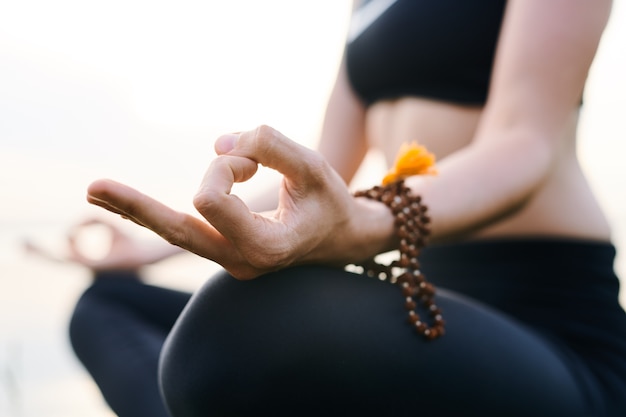 Close-up de irreconocible mujer concentrada en pensamientos vistiendo mala perlas en la muñeca meditando con las manos en mudra