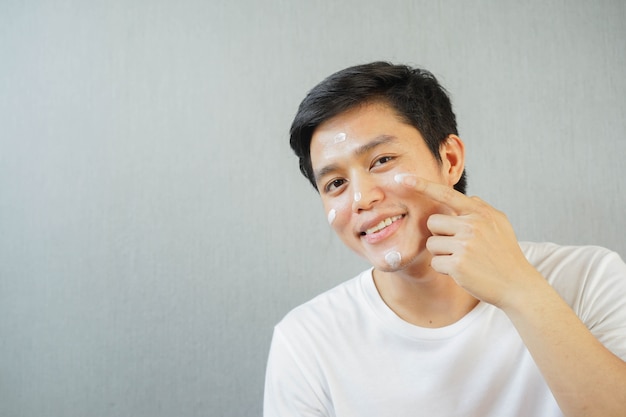 Close-up jovem asiático aplicando protetor solar UV no rosto