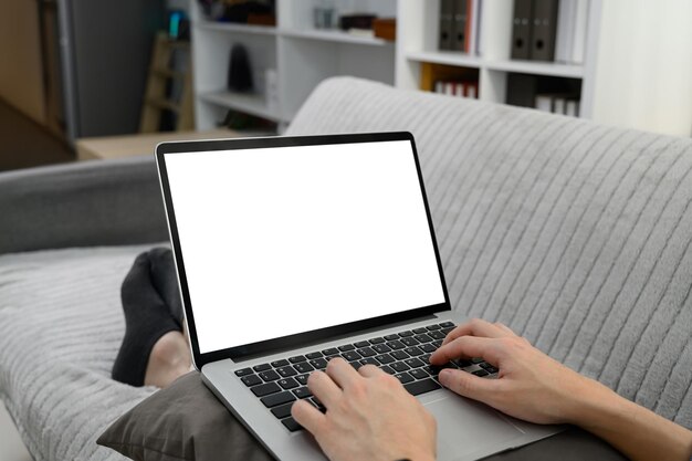 Close up de un joven escribiendo en una computadora portátil mientras está sentado en el sofá