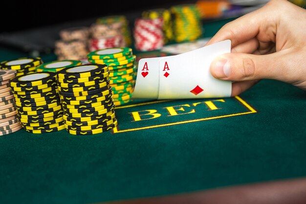 Close-up de jugador de póquer masculino levantando las esquinas de dos cartas de ases en la mesa de casino verde con ases