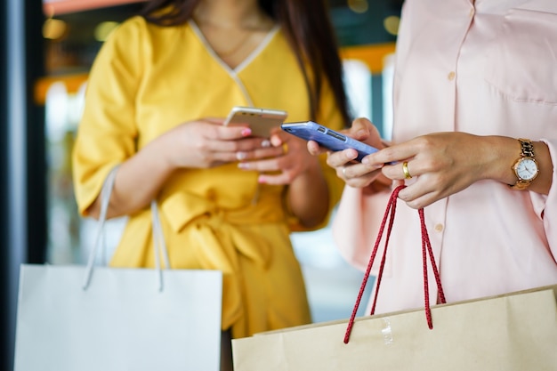 Foto close-up lindas mulheres asiáticas segurando o smartphone enquanto carregam sacos depois de terminar de fazer compras