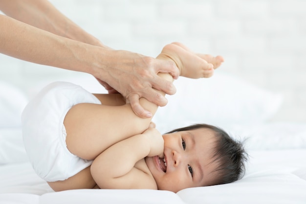 Close-up mãe mãos segurando a perna do bebê e exercício para saudável na cama sorrindo e felicidade emocional no quarto aconchegante, conceito de bebê saudável