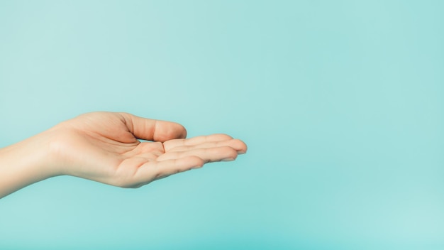 Close up de la mano de la mujer sosteniendo algo en fondo azul con espacio de copia