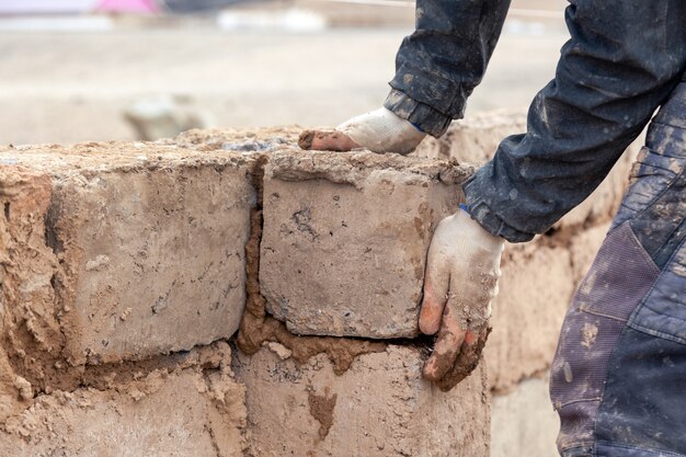 Close-up manos masculinas construir muro de casa sin terminar de ladrillo de arcilla