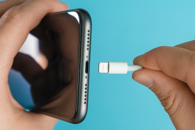 Foto close-up mão do homem inserindo um carregador na tomada do telefone móvel através de um cabo usb a relâmpago na superfície azul.