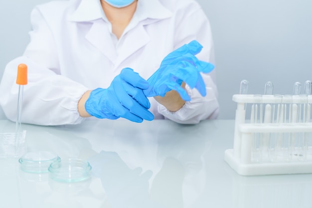 Close-up Mãos de cientistas colocando luvas de látex azul nitrílico em um jaleco usando luvas nitrílicas, fazendo experimentos em laboratório