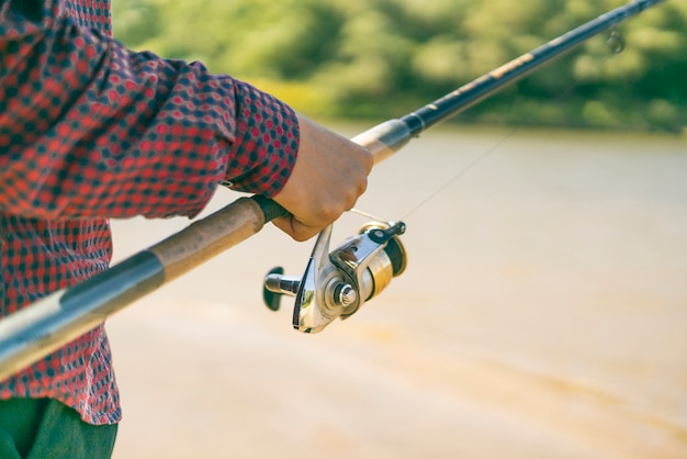 Foto close-up mãos masculinas pegando peixe com fiação na margem do rio.