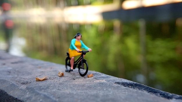 Close-up Minifigura Mulher brinca de bicicleta em River Side Path Way com espaço negativo ou cópia para a colocação da área de texto