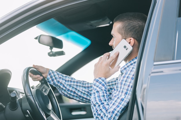 Close up.modern hombre hablando por un teléfono inteligente, sentado al volante de un coche.