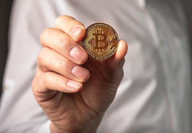 Close-up moeda de ouro bitcoin em mãos masculinas.