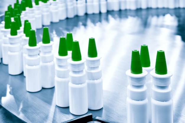 Close-up Muchas botellas de spray de plástico blanco para envasar medicamentos líquidos o cosméticos en una fila en una cinta transportadora en una fábrica de fabricación farmacéutica