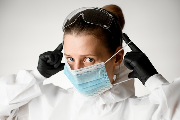 Close-up mujer en ropa protectora y guantes negros poniéndose una máscara en la cara