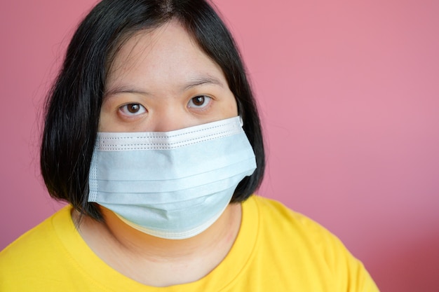 Close up - mujeres jóvenes con síndrome de Down con una máscara médica Ella es una estudiante de parálisis cerebral con un vestido amarillo