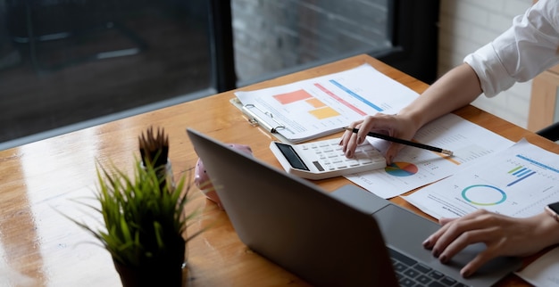 Close-up mulher de negócios usando calculadora e laptop para fazer finanças matemáticas na mesa de madeira no escritório e negócios trabalhando fundo, imposto, contabilidade, estatísticas e conceito de pesquisa analítica