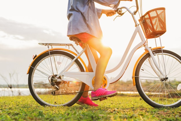 Foto close-up mulher de perna na bicicleta com pôr do sol no parque