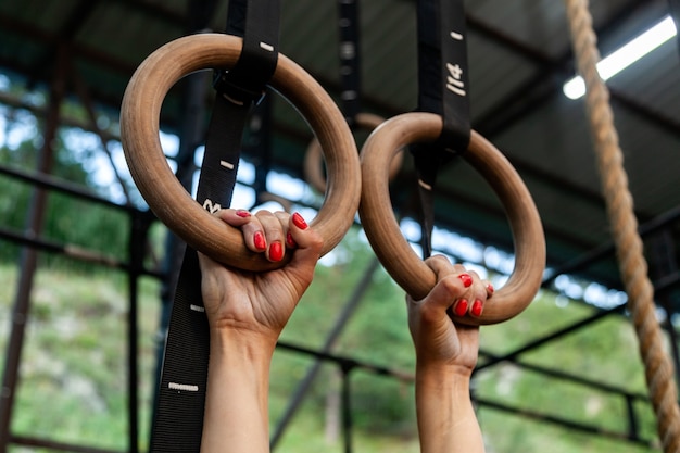 Close-up mulher jovem pendurada em anéis de ginástica, mãos em magnésia contra o pano de fundo da academia