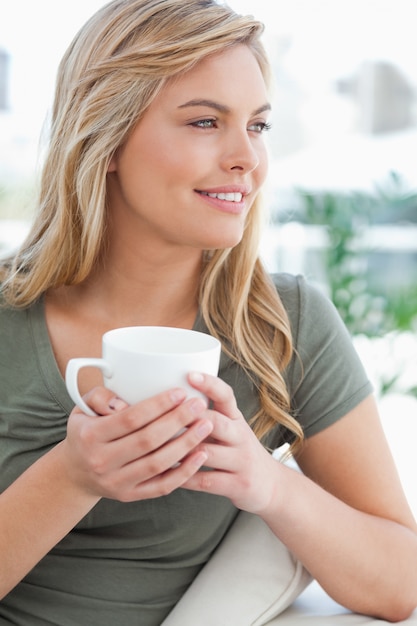 Close up, mulher segurando uma caneca nas mãos, a cabeça virada para o lado e sorrindo