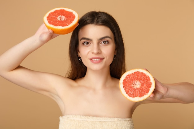 Close-up mulher seminua com pele perfeita maquiagem nude segura toranja isolada na parede bege