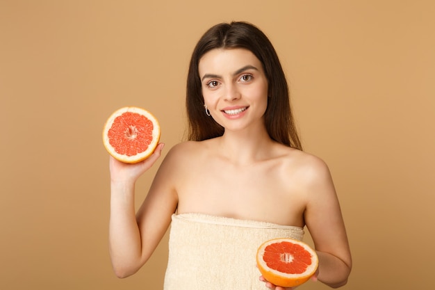 Close-up mulher seminua com pele perfeita maquiagem nude segura toranja isolada na parede bege