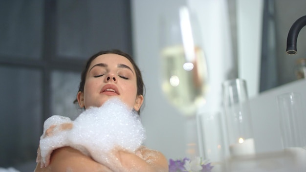 Close-up mulher sensual tocando o corpo com espuma na banheira Menina bonita relaxando no banho com espuma Mulher sexy lavando a pele no banheiro em câmera lenta