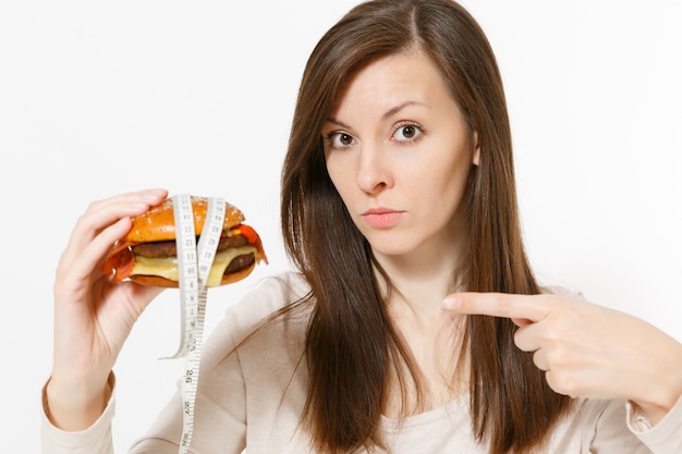 Close-up mulher tem nas mãos hambúrguer com alfaiate medindo fita isolada no fundo branco. Nutrição adequada ou fast food clássico americano. Copie o espaço para anúncio. Área de publicidade.