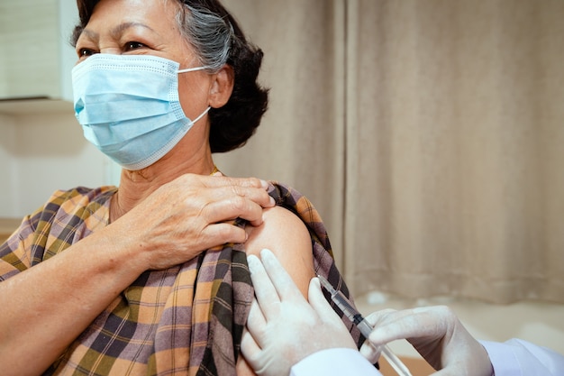 Close-up no médico é injetar vacinação no braço da mulher sênior. Paciente adulto usando máscara protetora para proteger o Coronavírus Covid-19 da pandemia. Cuidados de saúde e conceito médico.