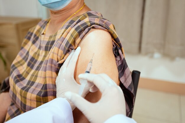 Close-up no médico é injetar vacinação no braço da mulher sênior. Paciente adulto usando máscara protetora para proteger o Coronavírus Covid-19 da pandemia. Cuidados de saúde e conceito médico.