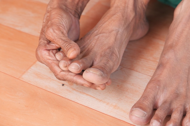 Close-up nos pés das mulheres sênior e massagem de mãos no local da lesão.