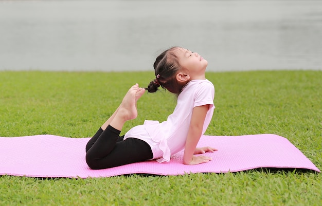 Close-up pequeña niña asiática niño haciendo yoga en el parque público.