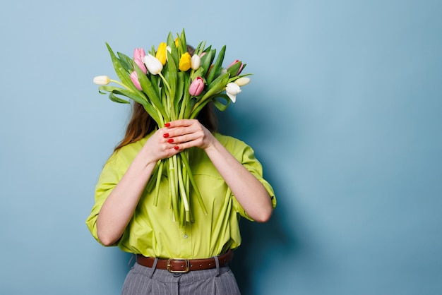 Close-up-Porträt einer Frau mit einem Blumenstrauß Tulpen an einem sauberen blauen Hintergrund Glückwunsch-Konzept